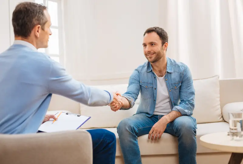 Two men shaking hands on couch.