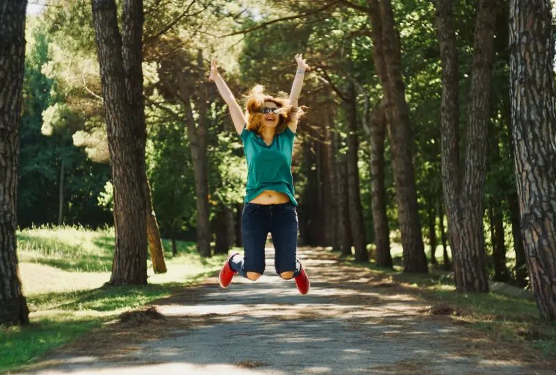 g 02 Person joyfully jumping on a forest path.