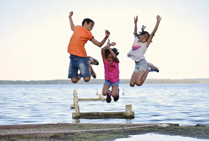 g 04 Children joyfully jumping near a lake.