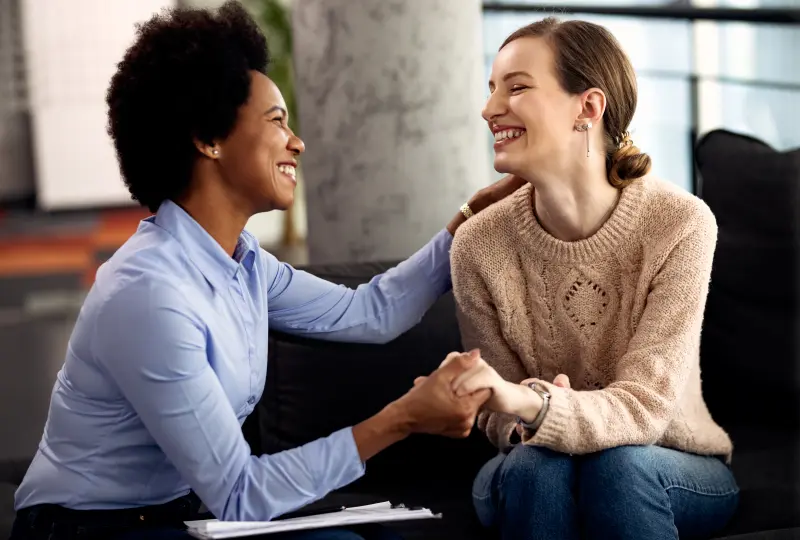 Two women smiling and holding hands warmly.
