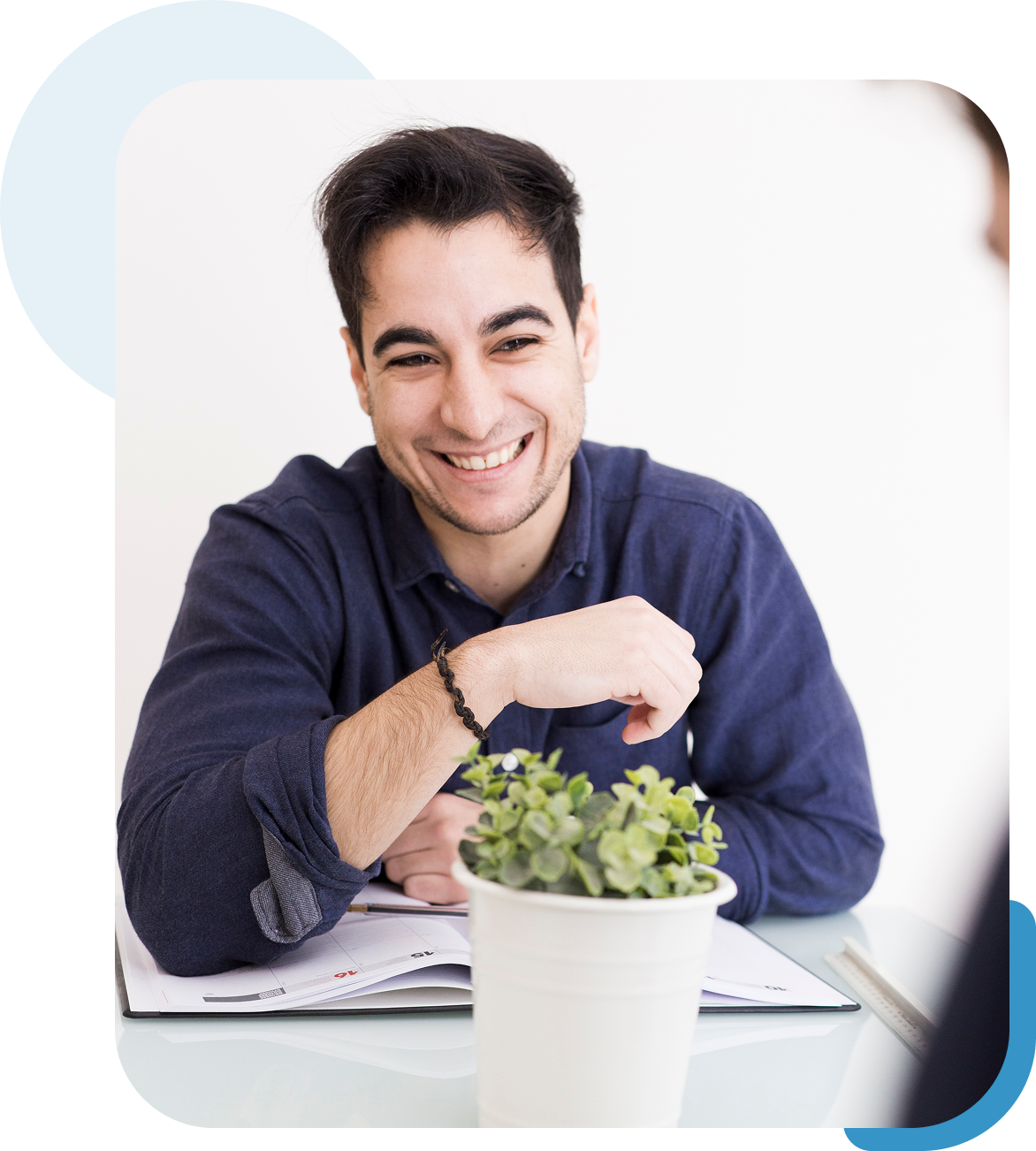 A smiling man sitting at a desk with a small plant.