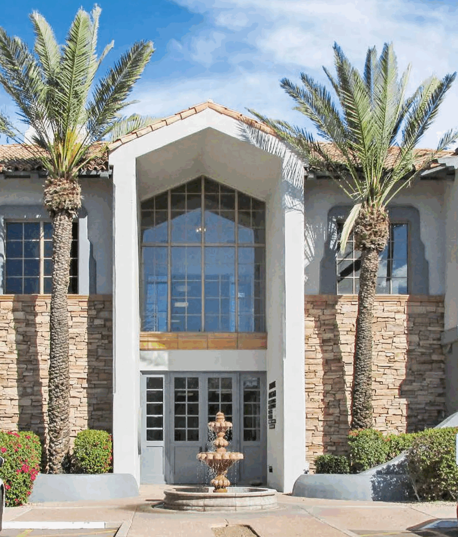 Elegant building entrance with tall palm trees and a water fountain.