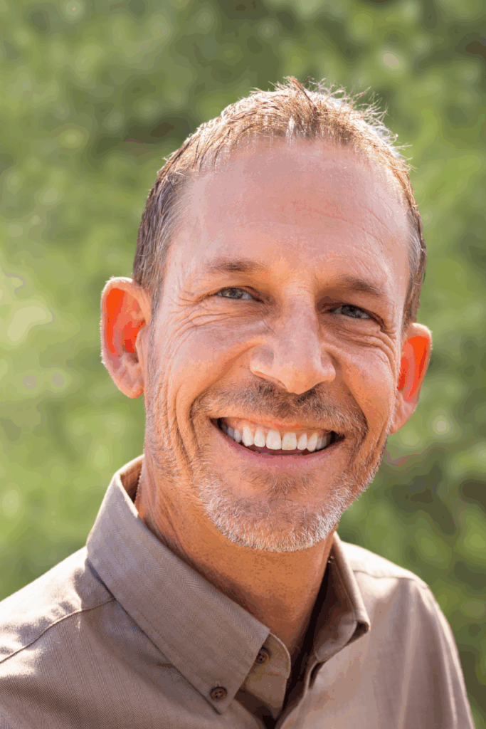 Smiling man outdoors with greenery background.