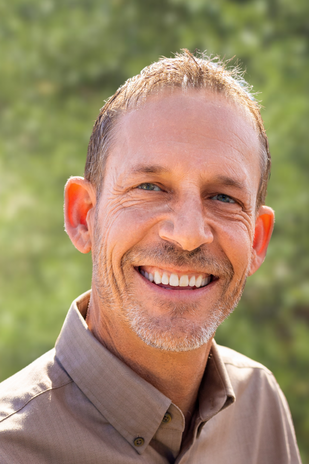 Smiling man outdoors with greenery background.