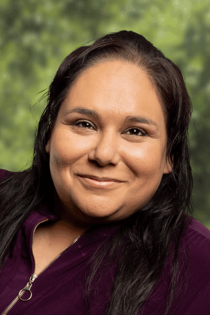 Portrait of a smiling woman with long dark hair against a green background.