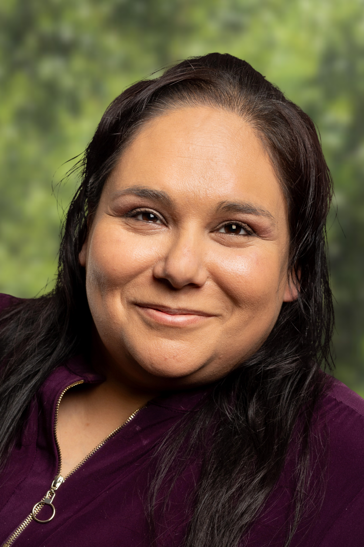 Portrait of a smiling woman with long dark hair against a green background.