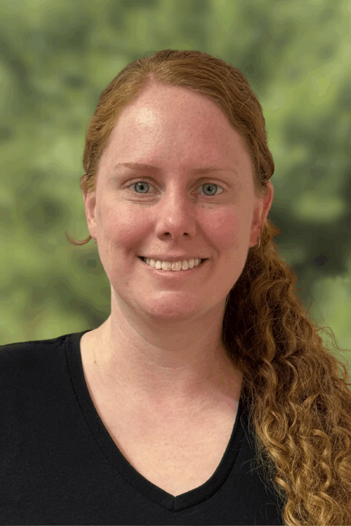 Smiling woman with curly red hair outdoors in natural light.
