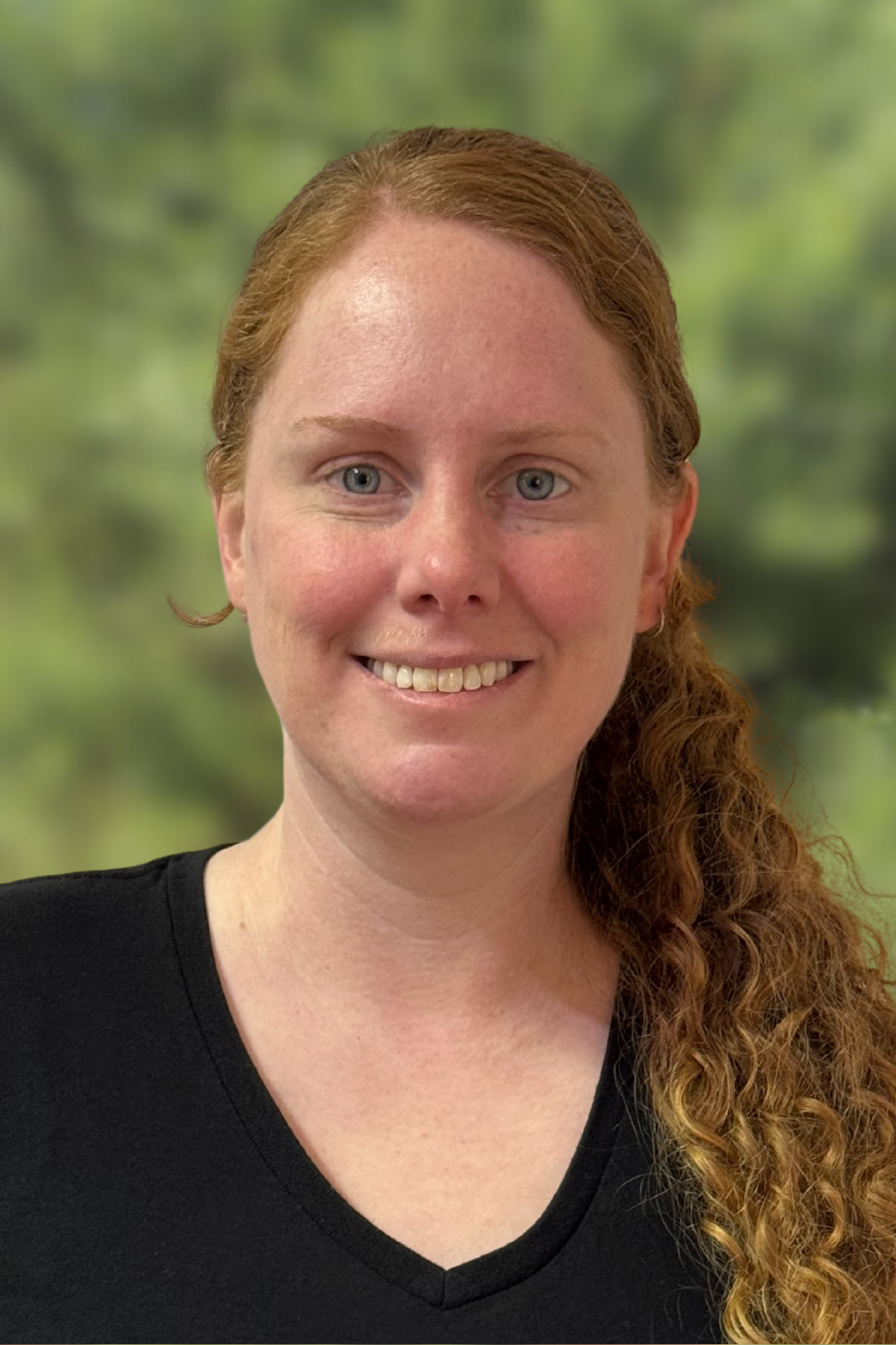 Smiling woman with curly red hair outdoors in natural light.