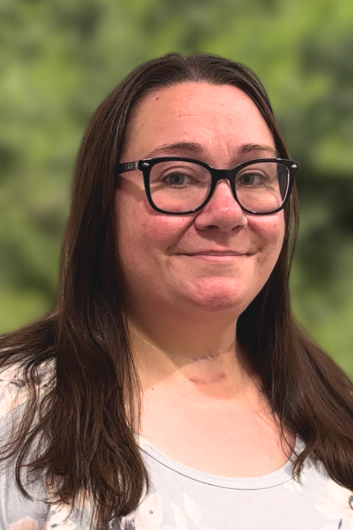 Smiling woman with glasses and long dark hair against a green blurred background.
