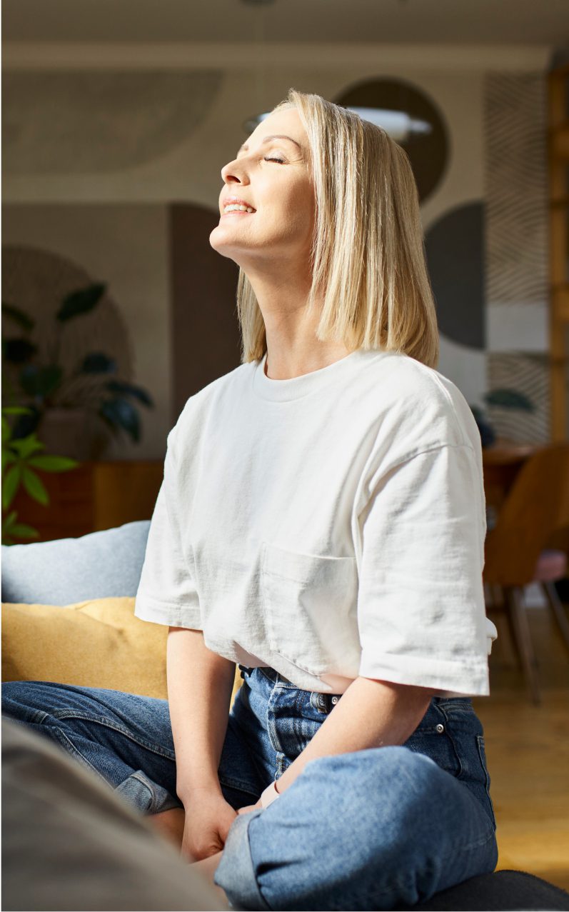 Woman smiling and sitting in sunlight indoors.